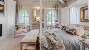 Een ruime slaapkamer met een groot bed, een bankje, een stoel en een open haard.