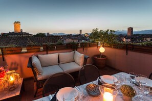 A rooftop terrace with a sofa, dining table set with plates and glasses, and a candle. - Casa Emy in Lucca With 3 Bedrooms and 2 Bathrooms (Lucca)