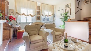 A living room with beige armchairs, a coffee table with a bottle of champagne, and a view of the city through large windows. - Casa Emy in Lucca With 3 Bedrooms and 2 Bathrooms (Lucca)