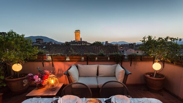 A rooftop terrace with a dining table set for two, a sofa, and potted plants. - Casa Emy in Lucca With 3 Bedrooms and 2 Bathrooms (Lucca)