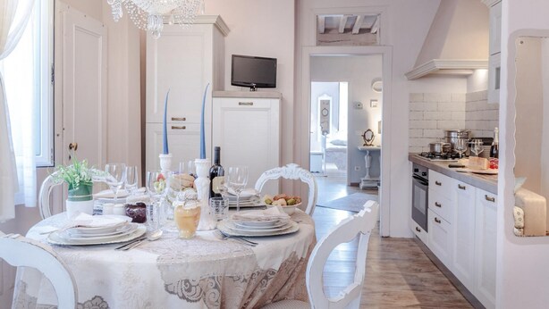 A dining area with a chandelier, a table set for a meal, and a kitchen in the background. - Casa Monique in Lucca (Lucca)