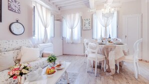 A cozy room with a floral sofa, a dining table set for two, and a chandelier. - Casa Monique in Lucca (Lucca)