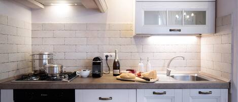 Une cuisine moderne avec des meubles blancs, une cuisinière à gaz, une machine à café et un évier.
