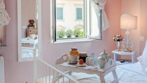 A pink-themed bedroom with a bed, a window with curtains, a bedside table, a mirror, and a birdcage with candles. - Casa Monique in Lucca (Lucca)