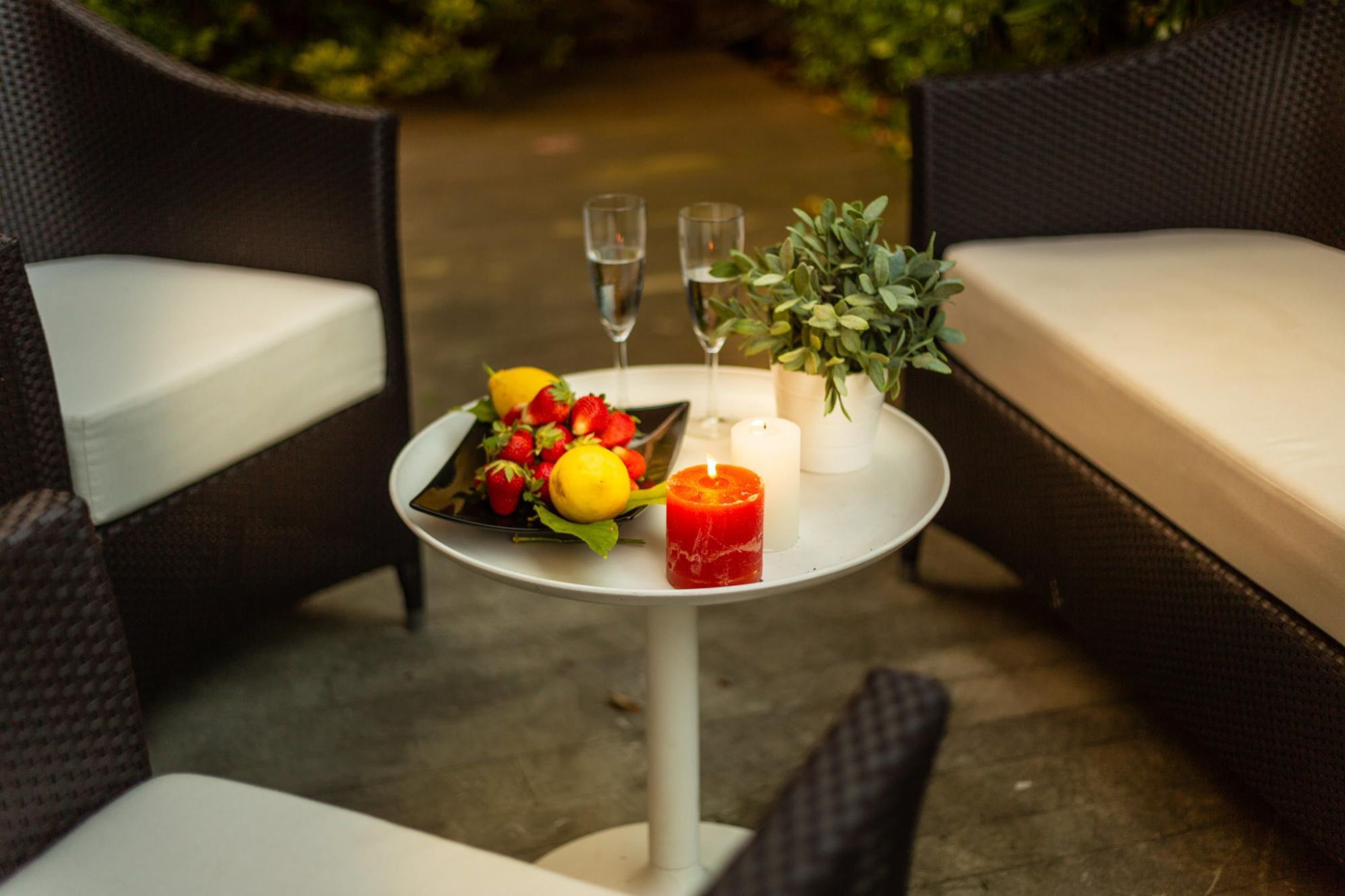 A table with a fruit platter, two glasses of water, a candle, and a potted plant.