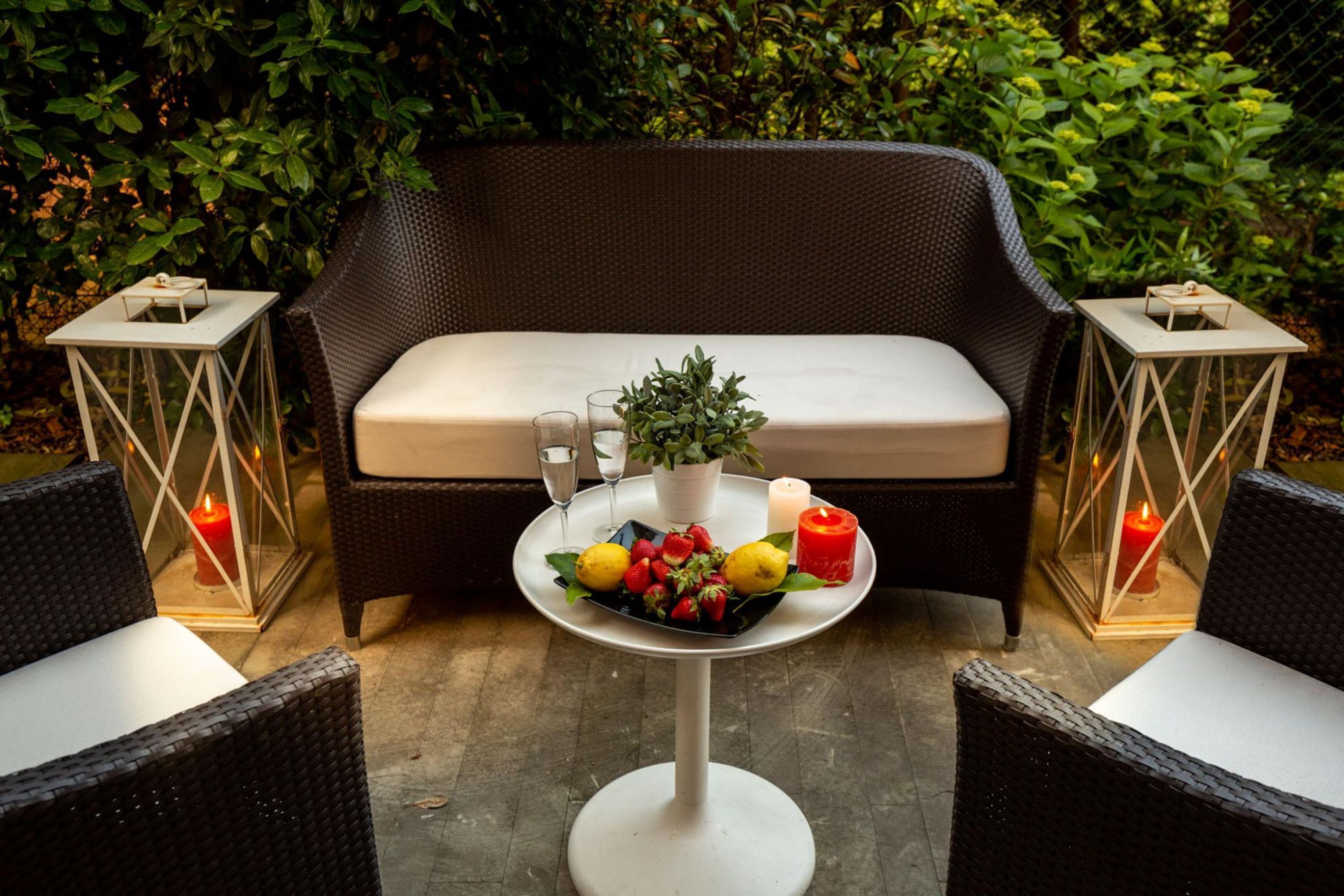 Een gezellig buitenzitje met rieten meubels, een tafel met fruit en kaarsen, en een comfortabele bank.