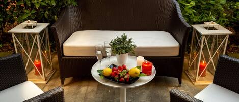 Een gezellig buitenzitje met rieten meubels, een tafel met fruit en kaarsen, en een comfortabele bank.