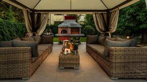 A covered outdoor seating area with wicker furniture and a central table with candles and fruit. - Villa Olivia in Lucca (Lucca)