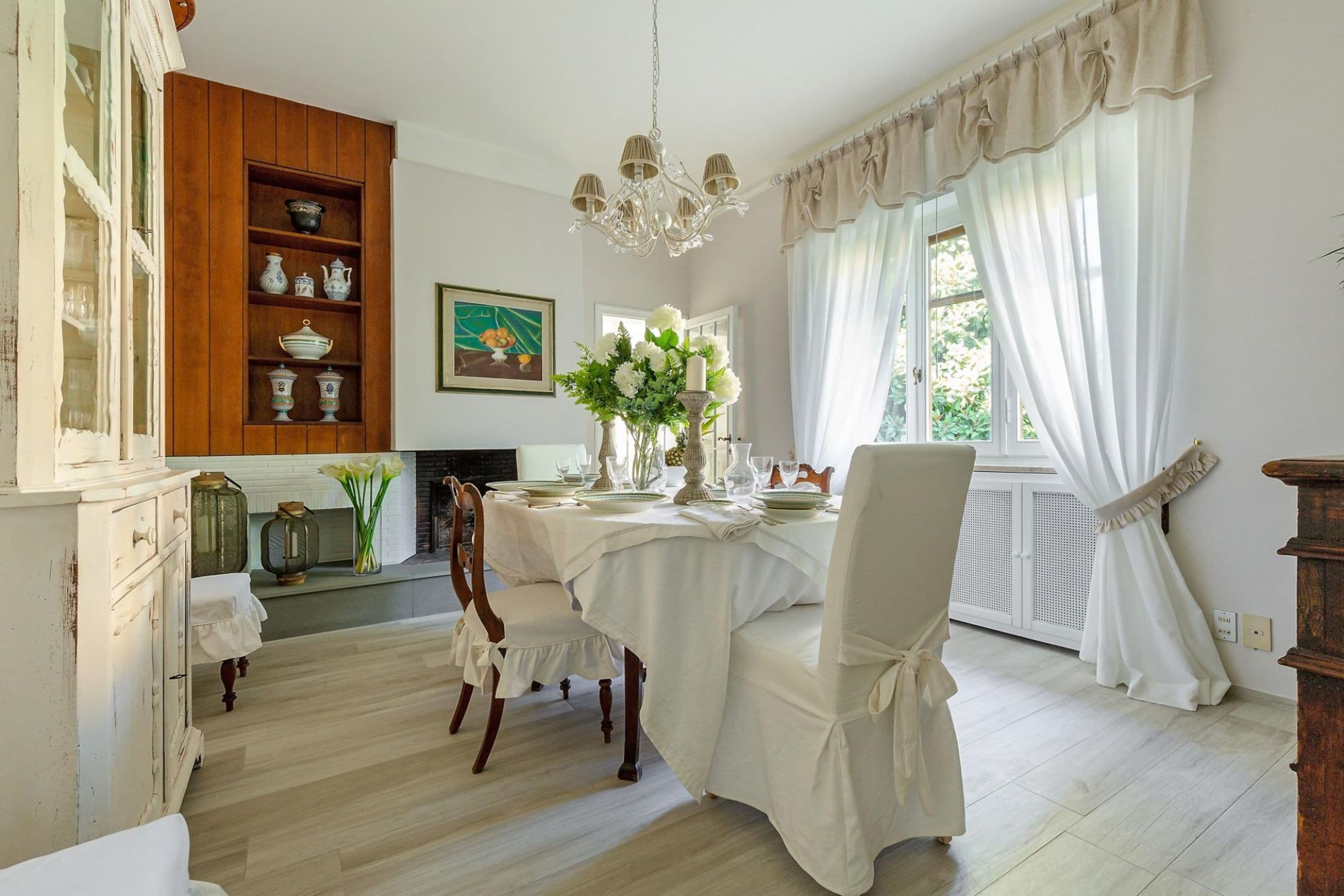 A dining area with a table set for four, a chandelier, and a bookshelf with decorative items.