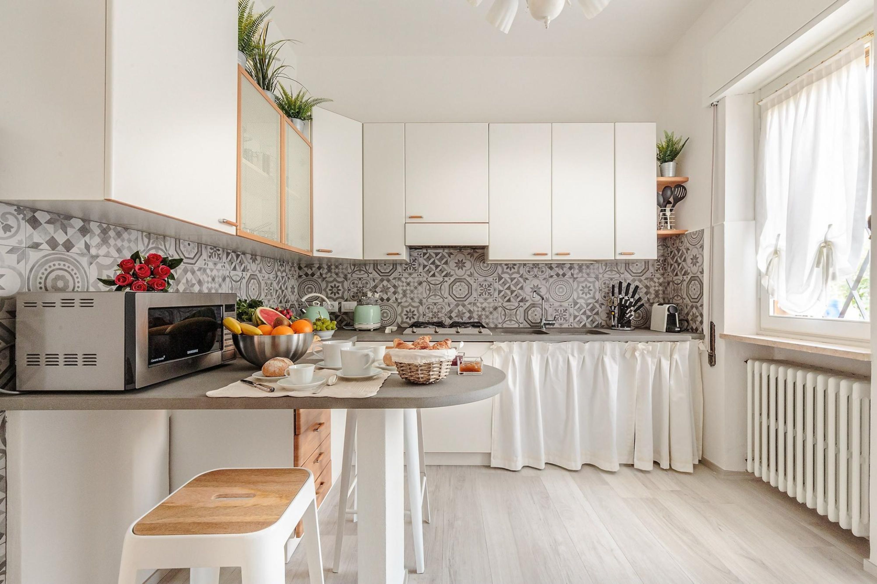 A modern kitchen with white cabinets, a microwave, a gas stove, and a dining area with a white table and bench.