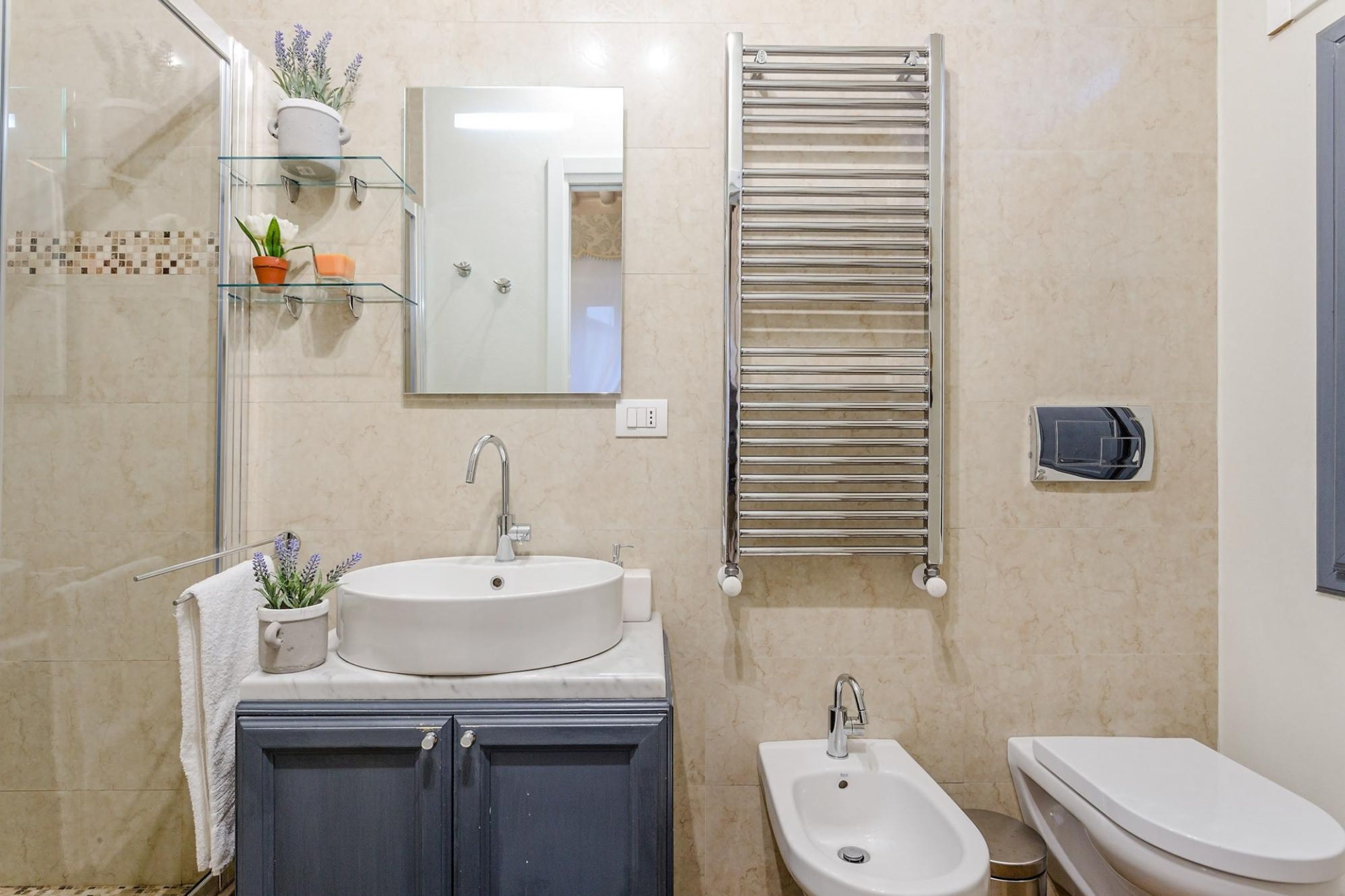 Ein modernes Badezimmer mit Duschkabine aus Glas, einem Waschbecken mit zwei Becken, einem Bidet und einem Handtuchhalter.