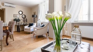 A well-lit living room with a dining area, featuring a vase of white flowers, a table with cups and a decorative lantern, and a large window with curtains. - Casa San Frediano in Lucca (Lucca)