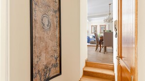 A hallway with a large framed artwork, wooden stairs leading to a dining area with a chandelier, and a wooden door. - Casa San Frediano in Lucca (Lucca)