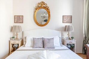 Een netjes opgemaakt slaapkamer met een groot bed, twee nachtkastjes, een kroonluchter en ingekaderde foto's aan de wand.