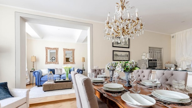 A dining area with a wooden table set for four, a chandelier, and a sofa in the background. - Casa San Frediano in Lucca (Lucca)