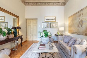 A living room with a white sofa, a coffee table with books, a large painting, and a mirror. - Casa San Giovanni in Lucca (Lucca)