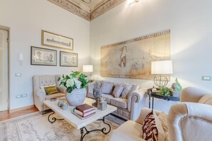 A living room with a sofa, coffee table, and decorative items. There are framed pictures on the wall and a large painting above the sofa. - Casa San Giovanni in Lucca (Lucca)