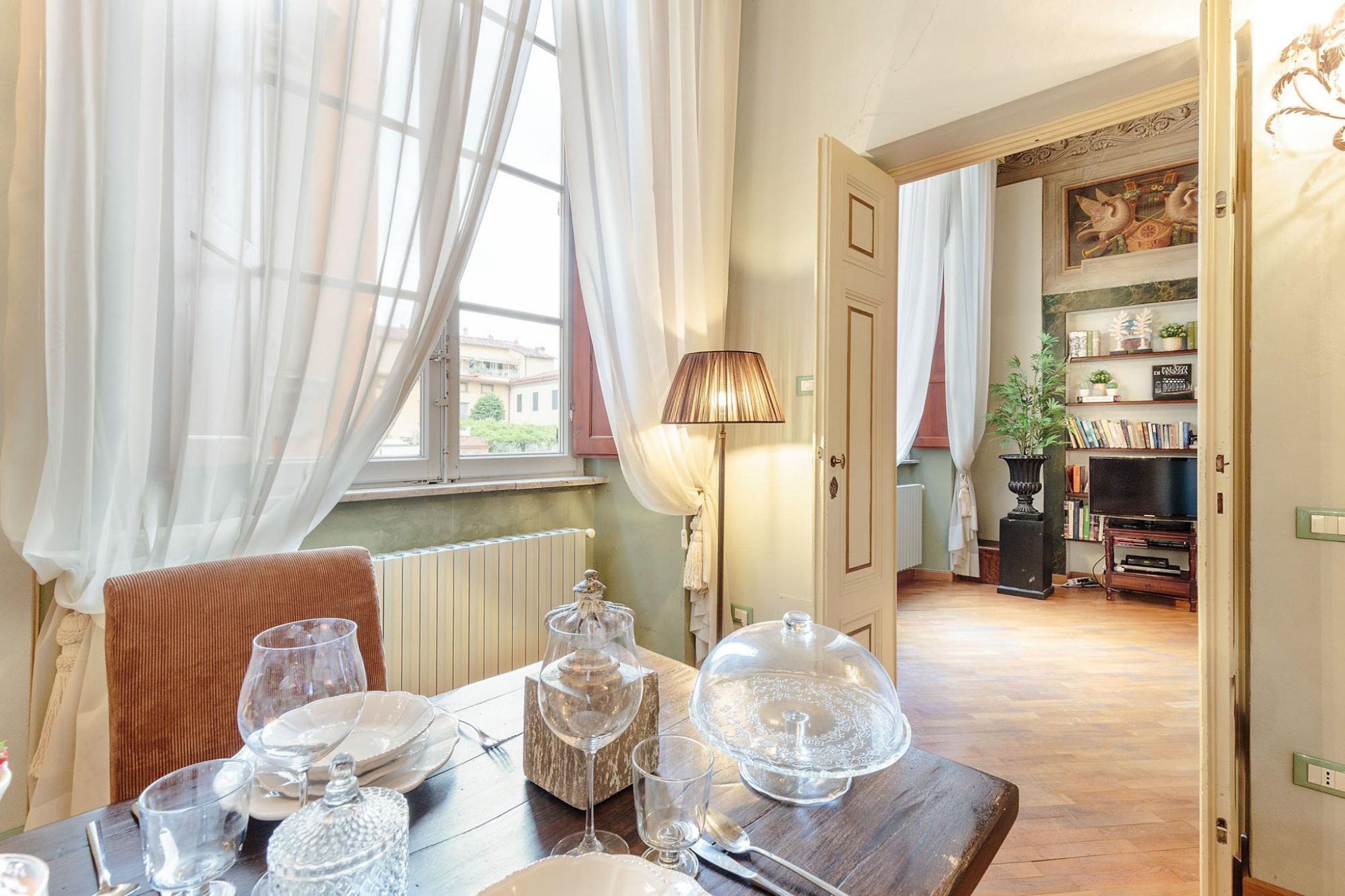 Ein Essbereich mit einem Tisch für vier Personen, einer Lampe und Blick auf die Straße durch große Fenster.