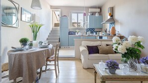 Eine moderne Küche mit hellblauen Schränken, ein Essbereich mit rundem Tisch und ein Wohnzimmer mit weißem Sofa.
