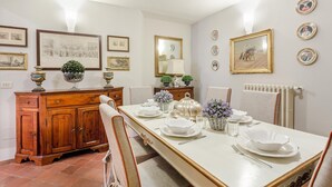 A dining room with a long table set for four, surrounded by chairs. There are framed pictures on the walls, a wooden cabinet, and a radiator. - Casa Simonetta in Lucca (Lucca)