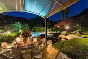 An outdoor patio with a table set for dining, surrounded by chairs, and a pool in the background. - Bicocche Stone Farmhouse (Camaiore)