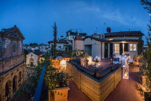 Terraço no telhado com móveis de vime, área de refeições e vista para edifícios ao redor.