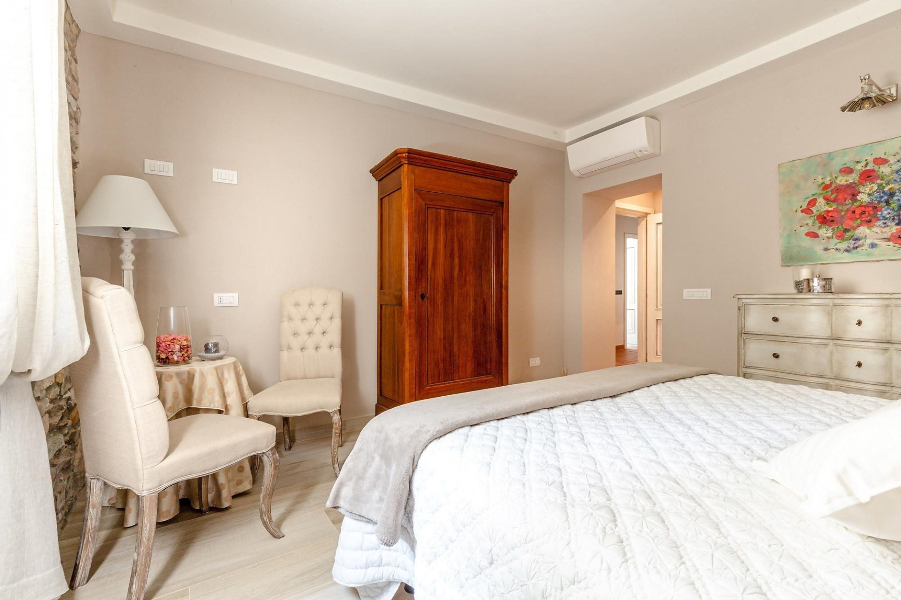 Une chambre avec un grand lit, une armoire en bois, une chaise, une petite table avec une lampe et un tableau accroché au mur.