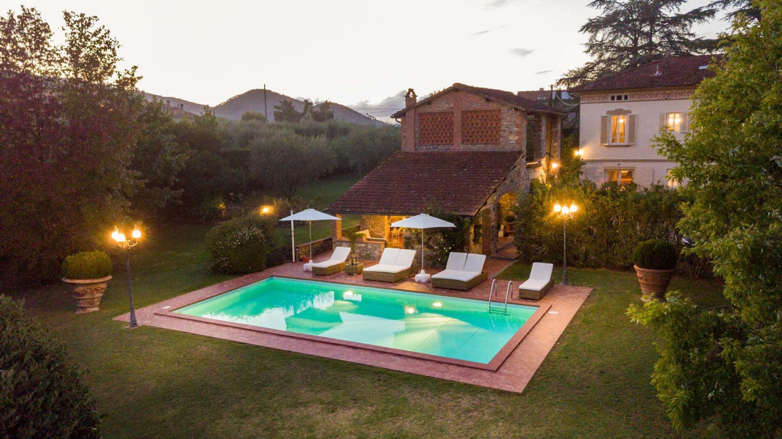 A swimming pool with lounge chairs and umbrellas, surrounded by a well-maintained lawn and trees.