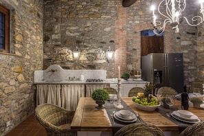 Enjoy meals in this charming dining area with a stone wall backdrop and a brick archway, featuring a dining table set with plates, silverware, and a fresh fruit centerpiece.