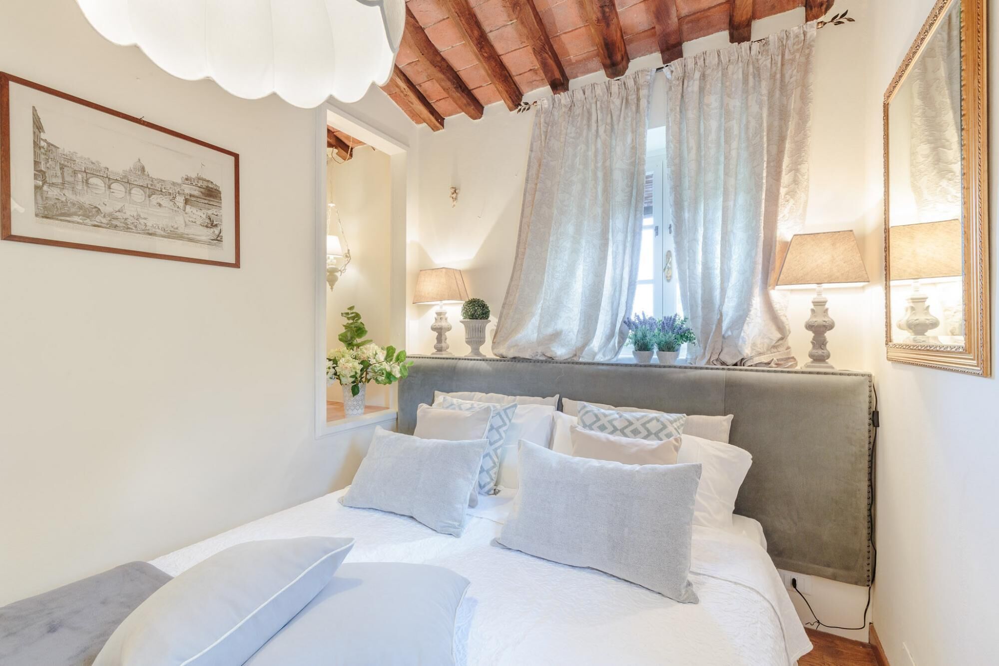 A bedroom with a bed, a large mirror, a window with curtains, and a painting on the wall.