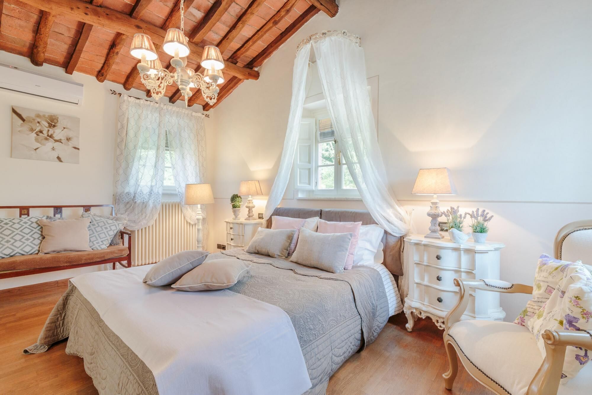 A bedroom with a wooden ceiling, a bed with a canopy, bedside lamps, a dresser, and a chair.