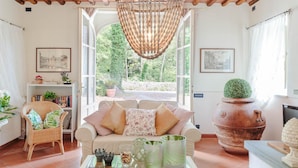 A cozy living room with a sofa, a coffee table, and a large window offering a view of greenery outside. - Villa Coccinelle in Pieve di Compito (Capannori)