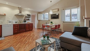 Um apartamento moderno com cozinha, sala de jantar e sala de estar. Possui piso de madeira, mesa de jantar com cadeiras vermelhas, um sofá cinza e uma televisão de tela plana fixada na parede.