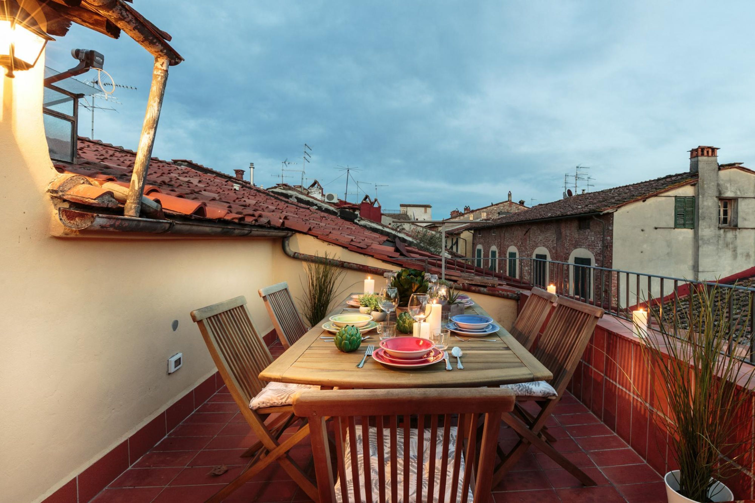 Ein Esstisch, gedeckt für ein Essen, auf einer Terrasse mit roten Fliesen, umgeben von Backgebäuden.