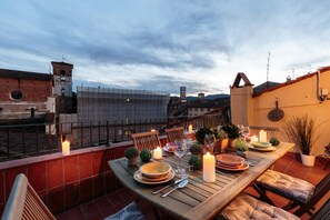 A rooftop terrace with a wooden table set for dining, surrounded by chairs, and adorned with candles and potted plants. - Terrazza Santa Croce (Lucca)