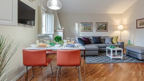 Uma sala de estar moderna com área de jantar, sofá cinza e uma pequena mesa com abajur.