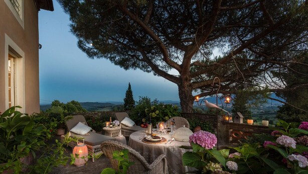 An outdoor dining area with wicker furniture, candles, and a view of the landscape. - Il Frantoio Farmhouse Apartment (Capannori)