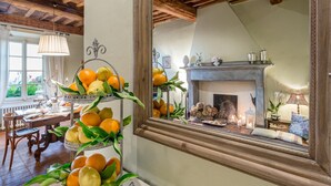 A cozy room with a fireplace, a dining table with chairs, and a fruit display. - Il Frantoio Farmhouse Apartment (Capannori)