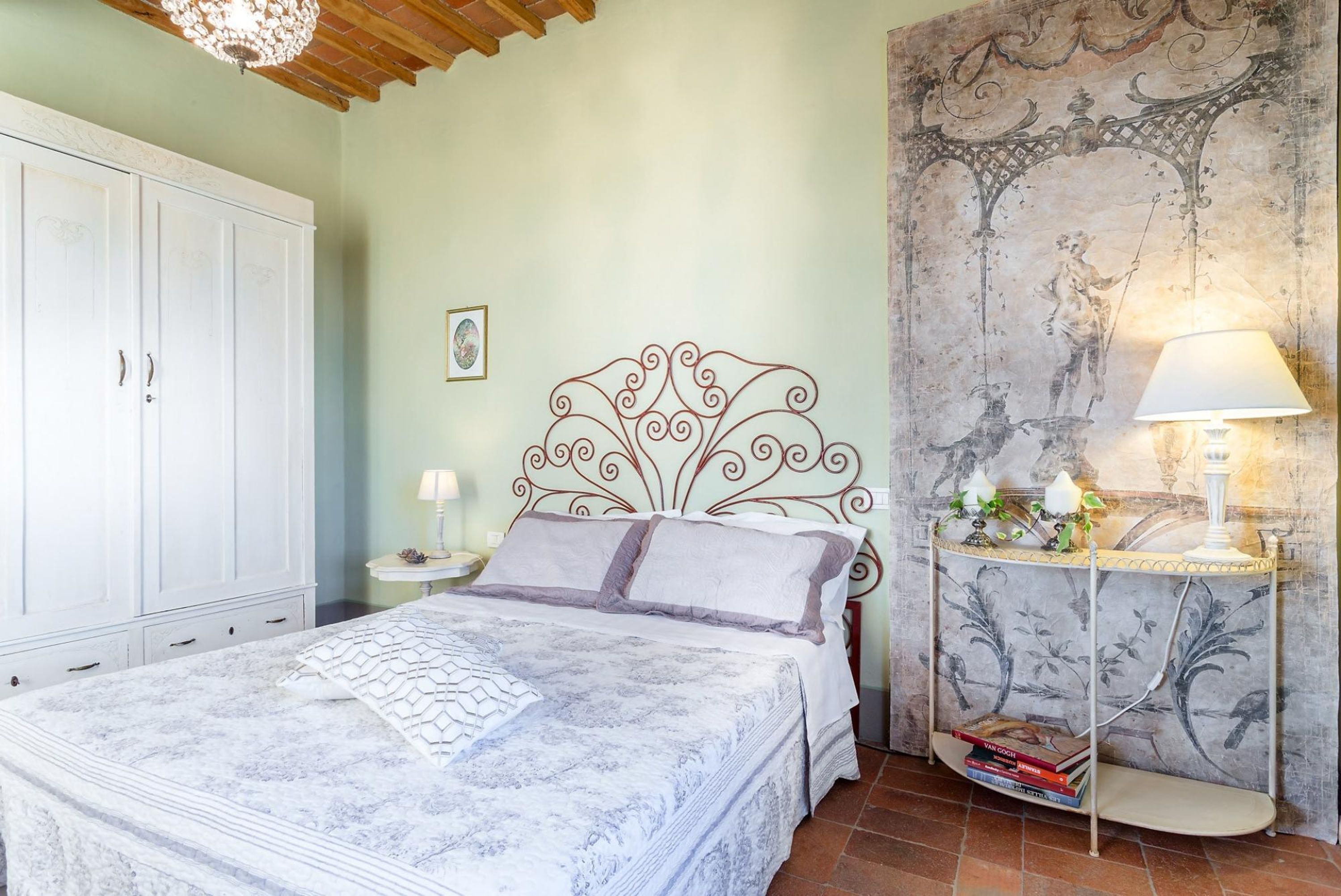 A bedroom with a bed, a nightstand, a lamp, a wardrobe, and a decorative wall.
