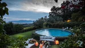 A circular pool with a surrounding seating area, including a sofa and lounge chairs, and a view of distant city lights. - Il Frantoio Farmhouse Apartment (Capannori)