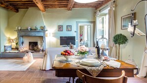 A dining area with a wooden table set for four, a fireplace, and a television in the background. - Il Frantoio Farmhouse Apartment (Capannori)