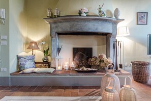 Cozy living room with a fireplace, featuring a vase, sculpture, and candles, as well as a lamp, bench, and wicker basket.