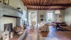 A cozy living room with a fireplace, a dining area, and a view of the outdoors. - Il Frantoio Farmhouse Apartment (Capannori)