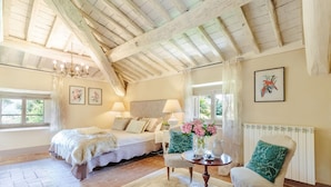 A bedroom with a bed, a chair, a table with flowers, and a radiator. - Villa Gattaiola in Gattaiola (Lucca)