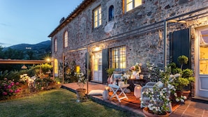 A stone building with a well-maintained garden, outdoor seating, and a visible entrance. - Villa Il Palagio in Capannori (Capannori)