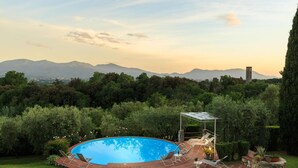Ein Pool mit Terrassenbereich, umgeben von üppiger Vegetation und Blick auf ferne Berge.
