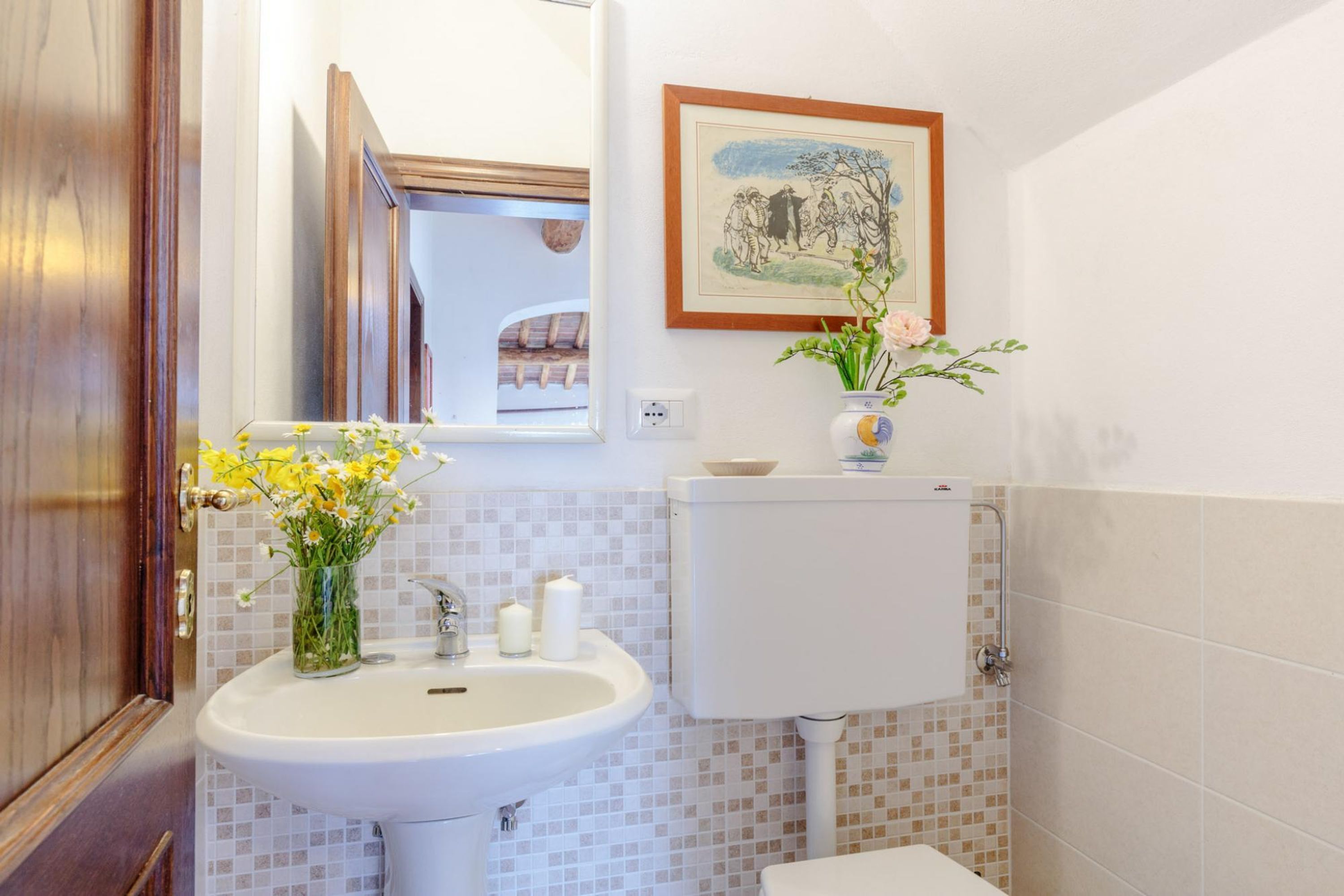 A bathroom with a white sink, a mirror, a toilet, and a framed picture on the wall.