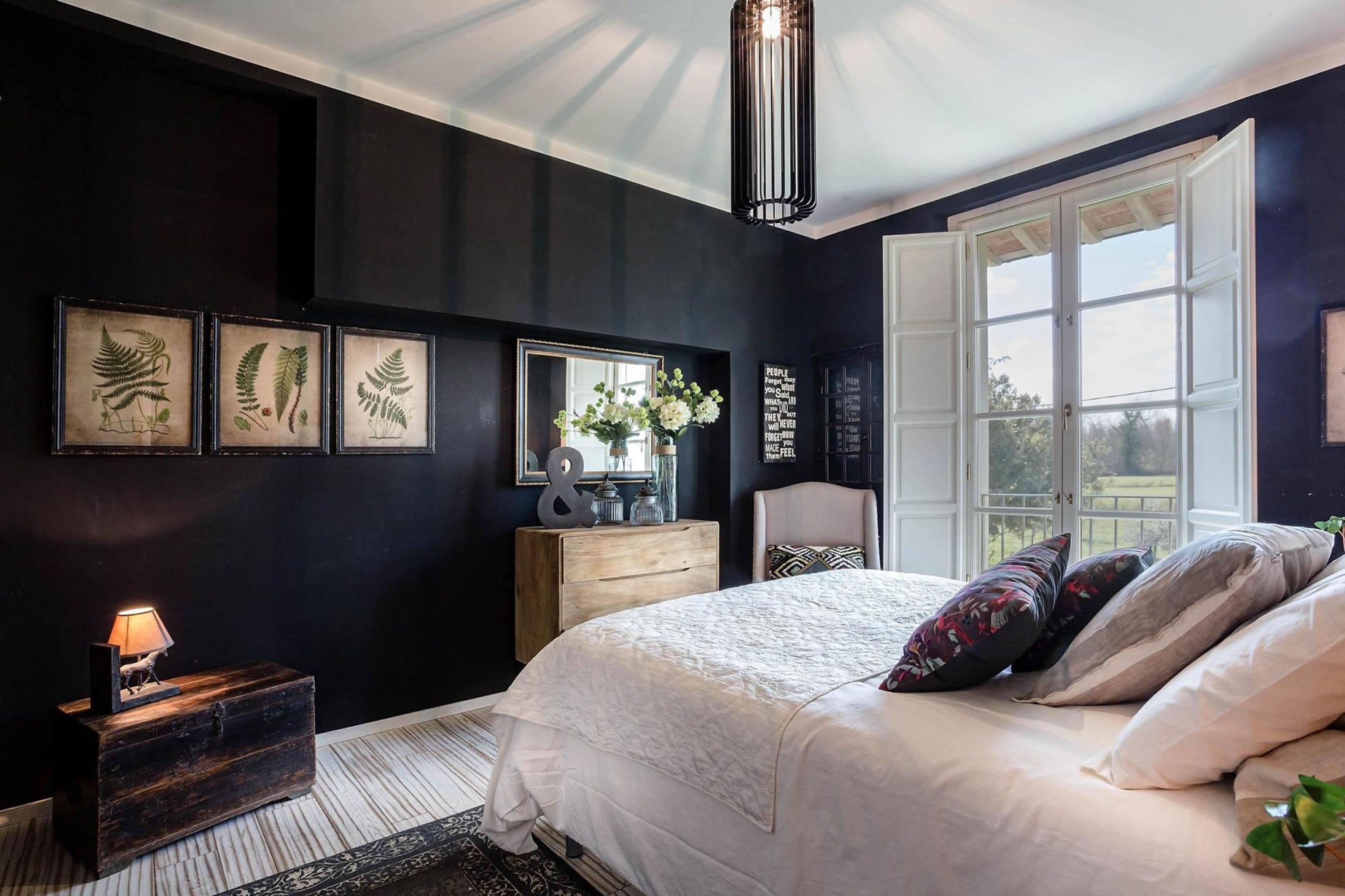 A bedroom with a large bed, a dresser, a mirror, and framed botanical prints on the wall.