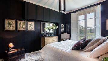 A bedroom with a large bed, a dresser, a mirror, and framed botanical prints on the wall.