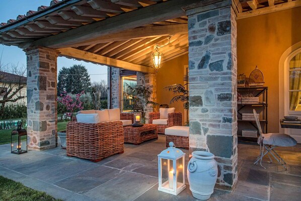 A covered outdoor seating area with stone pillars, wicker furniture, and lanterns. - Villa Otto in Orentano (Castelfranco di Sotto)